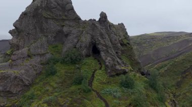 Sivri yosunlu bir uçurumun etrafındaki drone yörüngesi sisli gökyüzünün altında geniş bir volkanik kanyonu ortaya çıkarıyor..