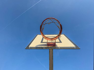 Dikdörtgen bir basketbol potasının alçak açılı görüntüsü ve parlak bir gökyüzünün altında metal bir halka..