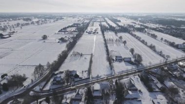 Uçsuz bucaksız kış manzarası, karla kaplı tarlalar, çiftlik evleri ve güneş ışığındaki uzun gölgeler..