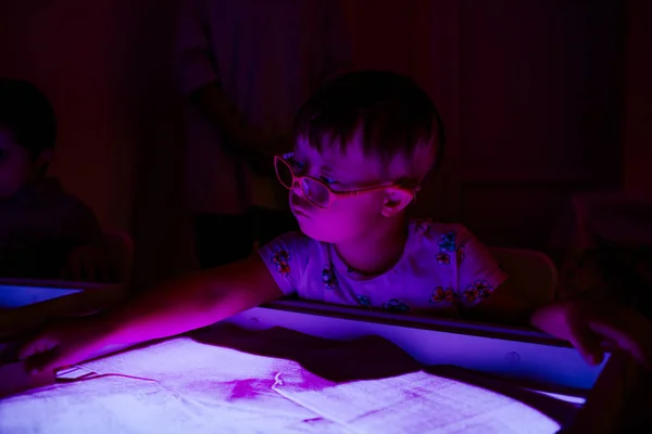 Child with Down syndrome is engaged in sand therapy on a light table with lights. High quality photo