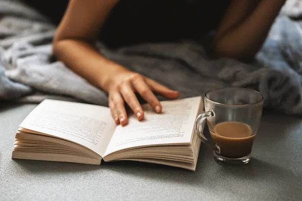 Young girl reading an interesting book and dinking a fresh cup of coffee in her free time.