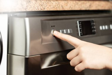 Bulaşık makinesinin düğmelerine basan genç bir kadın. Kız bulaşık makinesini çalıştırmaya çalışıyor..