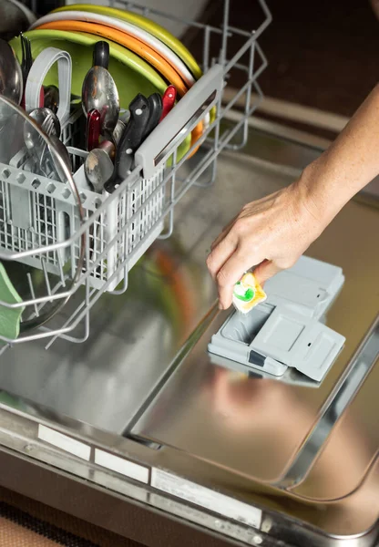 Bulaşık makinesini açmaya çalışan genç bir kadın. Kadın temizlik yastığını bulaşık makinesine koyuyor..