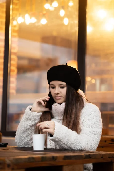 Genç kız telefonuyla konuşurken kahve içiyor. Sıcak bir restoranda kahve içen bir kız..