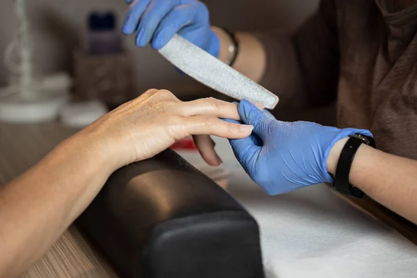 Closeup shot of a woman in a nail salon receiving a manicure by a butician with nail file. Woman getting nail manicure. Butician file nails to a customer.