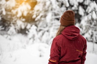 Genç kız karlı ormanda bir şey izliyor. Karlı dağlar.