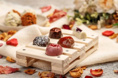 Beyaz ahşap arka planda küçük el yapımı çikolatalar, yapraklarla çevrili..