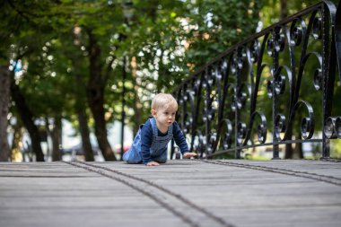 Küçük sarı saçlı bebek köprüden tırmanıyor. Mutlu bebek.