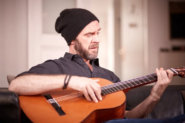 Мужчина с бородой играет дома на гитаре — стоковое фото