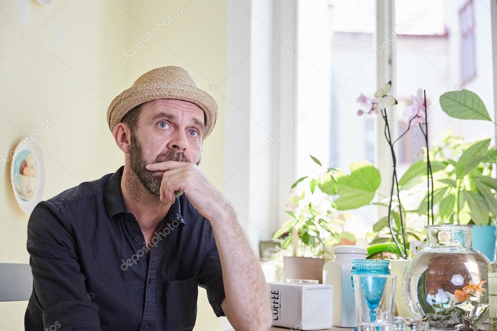 Man with hat and beard sitting and pondering