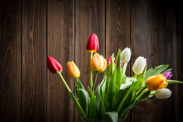 Barevné tulipány ve váze na dřevěný stůl — Stock fotografie