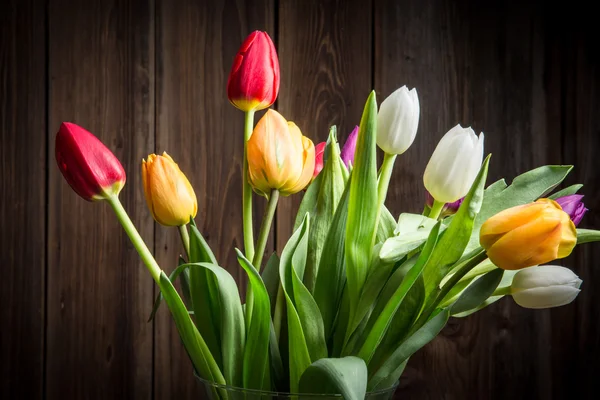 Barevné tulipány ve váze na dřevěný stůl — Stock fotografie