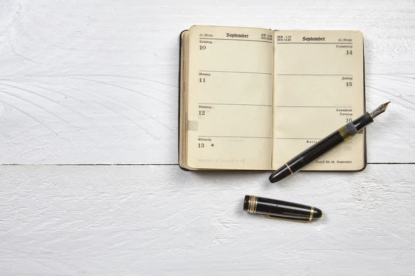 Caneta-tinteiro antiga e calendário antigo em uma mesa de madeira branca — Fotografia de Stock