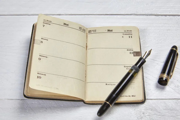 Caneta-tinteiro antiga e calendário antigo em uma mesa de madeira branca — Fotografia de Stock