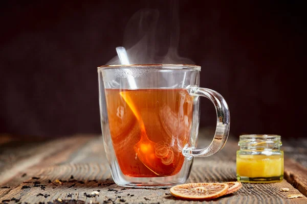 Steaming earl grey tea and a pot of honey and oranges on a wooden table