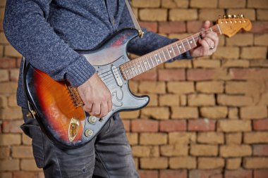 Müzisyen tuğla duvar önünde gitar oynuyor