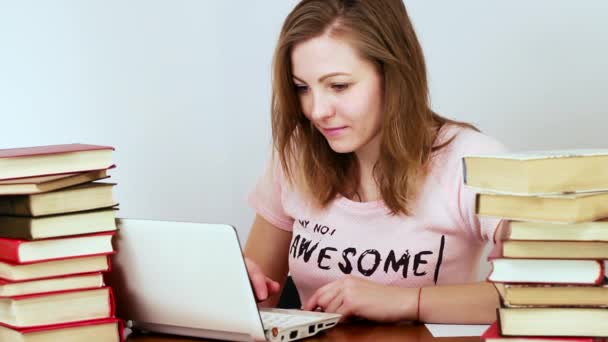 Hübsches Mädchen, das an einem Laptop in der Universität arbeitet. um sie herum viele Bücher. — Stockvideo