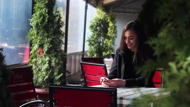 Menina muito bonita está digitando uma mensagem em um smartphone sentado em um restaurante . — Vídeo de Stock