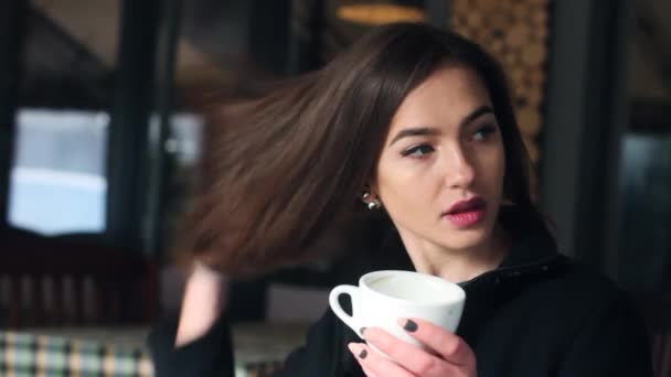 Sehr süßes und schönes Mädchen trinkt Kaffee und schaut in die Kamera. das Mädchen im Café. — Stockvideo
