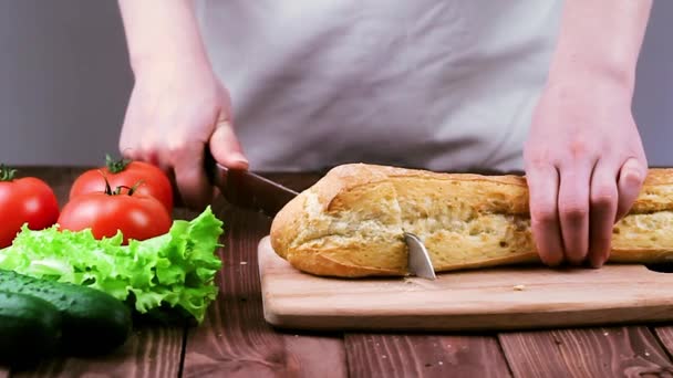 Cook skära baguette på en bräda i restaurangen. på bordet låg tomater, sallad och gurkor. Slow motion — Stockvideo