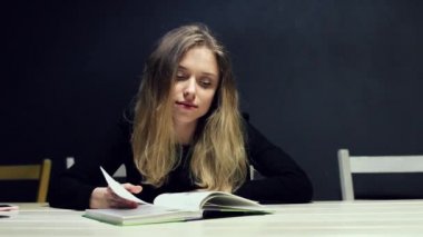 Güzel kadın Üniversitesi kitaplığındaki bir masada otururken bir kitap okuma. Kız öğrenci bir kitabın sayfalarını açar ve gülümseyen.
