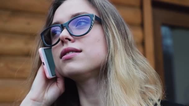 Hermosa chica con gafas, hablando por teléfono fuera de la oficina. las Sonrisas de las chicas. Ella es muy feliz y amable . — Vídeo de stock