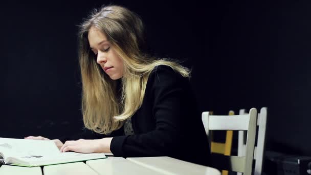 Όμορφη γυναίκα διαβάζοντας ένα βιβλίο, ενώ κάθεται στο τραπέζι. Κορίτσι φοιτητής. — Αρχείο Βίντεο