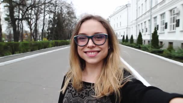 Très belle et gentille fille en lunettes fait Selfie près du bureau. Femme souriante et photographiée elle-même au téléphone. Elle est heureuse. . — Video