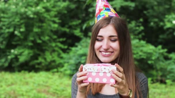 Bella donna che apre un regalo di compleanno. una donna molto felice. Ragazza in piedi in un cappello celebrativo. Lei piace . — Video Stock