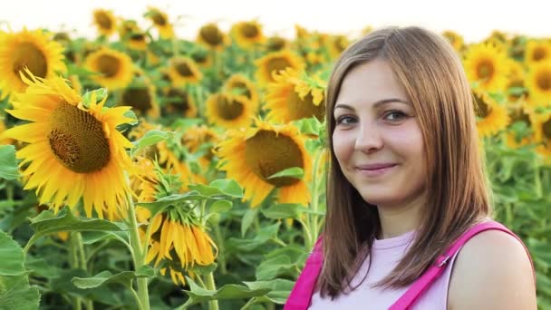 Ein Mädchen mit einer Flasche Sonnenblumenöl in der Hand. Eine Frau steht mit Sonnenblumen auf dem Feld. sie ist sehr schön und lächelt. — Stockvideo