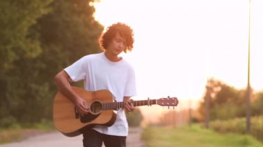 Adam günbatımı ve gitar çalmak yolda bir müzisyendir. Adam kıvırcık saç.
