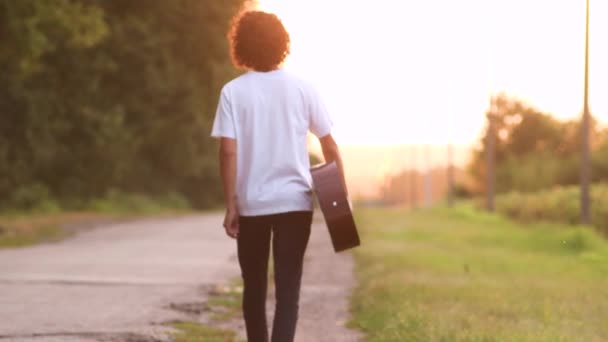 El chico con un caminante de guitarra. él está en el camino al atardecer . — Vídeos de Stock