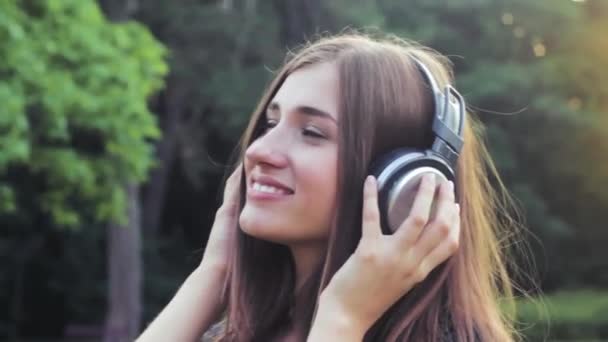 Krásná dívka poslouchá hudbu v parku při západu slunce. — Stock video
