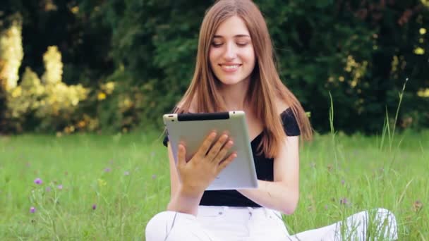 Krásná dívka pracuje na tabletu zatímco sedí v parku. Zpomalený pohyb — Stock video