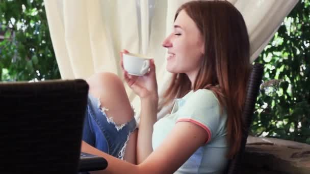 Hermosa chica tomando café en un restaurante y sonriendo alegremente. La chica se sienta a la mesa. Ella es muy linda y atractiva. . — Vídeos de Stock