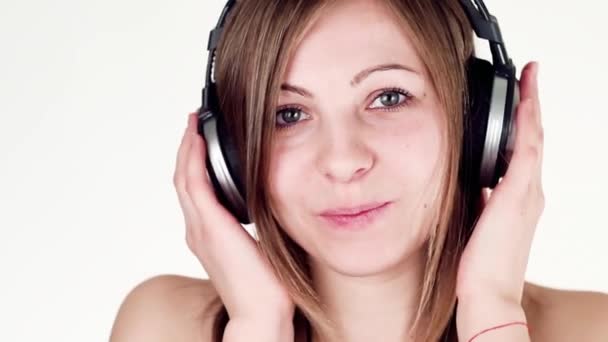 Hermosa y alegre chica escuchando música con auriculares, bailando y mirando a la cámara — Vídeo de stock