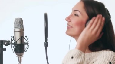 Komik ve güzel bir kız bir kayıt stüdyosunda şarkı söylüyor. Kız beyaz bir arka plan üzerinde kulaklık giyiyor.