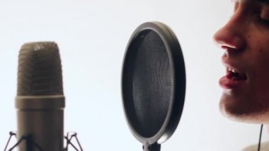 Sevimli şarkıcı şarkıyı bir kayıt stüdyosunda kaydetti. Mikrofona şarkı söyleyen adam. Beyaz bir arka plan üzerinde duruyor. Arka.