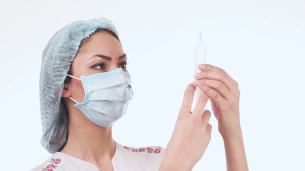 Beautiful, young nurse prepares an injection. A girl holding a syringe, standing in a mask and medical cap. — Stock Video