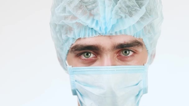 Un joven doctor mirando la cámara. Es muy grave. Doctor con gorra médica y máscara. De cerca. . — Vídeos de Stock