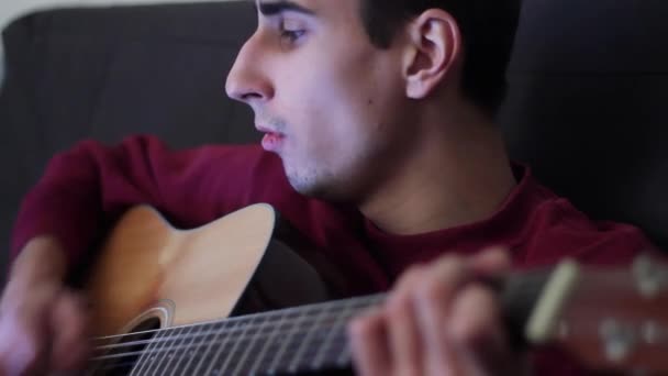 Den begåvade och vackra musiker spelar akustisk gitarr i mörkret. Killen sjunger och spelar. Närbild. — Stockvideo