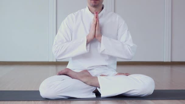 Um homem vestido de branco pratica ioga. Ele dobrou seus braços e namaste meditando. Ardha Padmasana — Vídeo de Stock