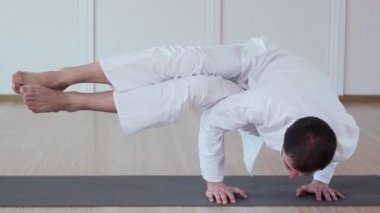 Bir adam yoga uygulamaları. Astavakrasana. Yogi beyaz bir elbise giymiş.