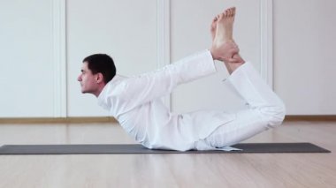 Dhanurasana.Man Yogi uygulamaları Yoga. Beyaz bir elbise giyiniyor.