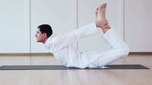 Dhanurasana.Man Yogi pratique le Yoga. Il est vêtu d'une robe blanche . — Video