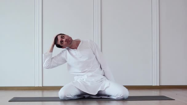 Lindo tipo haciendo yoga. Se sienta con un traje blanco. . — Vídeos de Stock