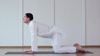 Şirin çocuk Yoga yapıyor. Beyaz takım elbiseli oturuyor. Marjari Asana