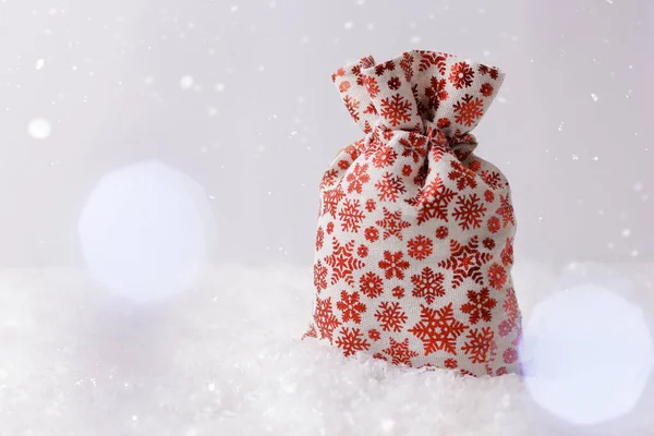 Christmas holidays backdrop with gift bag, snow, bokeh and copy space for text. Christmas gift bag with red snowflakes.