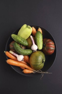 Black plate variety of raw vegetables ready to cook fresh natural vegetables on black background.