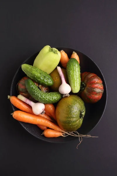 Black plate variety of raw vegetables ready to cook fresh natural vegetables on black background.